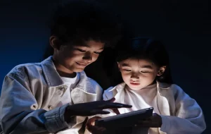 Τwo kids sitting in a dark room and looking with interest to internet on digital pad