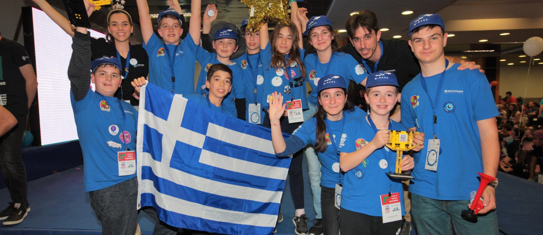 O κύριος Περλαντίδης και η κυρία Αποστολία μαζί με μια ομάδα δέκα μαθητών των εκπαιδευτηρίων ντυμένων στα μπλέ, σηκώνουν τα κύπελα κρατώντας την ελληνική σημαία