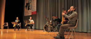 four men playing musical instruments on the stage of mandoulides schools