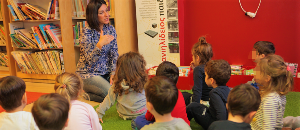 Students of the kindergarten of mandoulides schools sitting and listening to teacher at Daniilideios Children's Library
