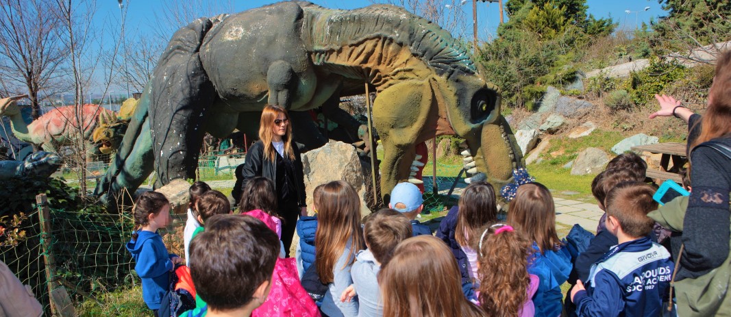 Τα νήπια των εκπαιδευτηρίων μαντουλίδη κοιτάζουν έναν τυρανόσαυρο ρεξ καθώς η ξεναγός τους εξηγεί λεπτομέρειες για τον δεινόσαυρο