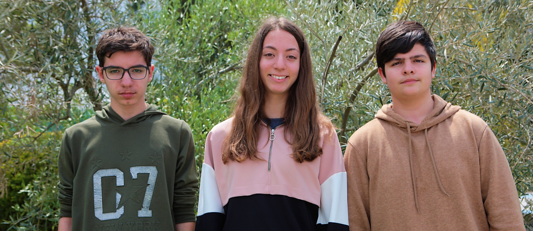Οι 3 μαθητές των εκπαιδευτηρίων που που πέρασαν στον Πανελλήνιο Τελικό του Παγκοσμίου Πρωταθλήματος της Microsoft , 2 αγόρια και ανάμεσα τους ένα κορίτσι, χαμογελούν με πράσινο φόντο