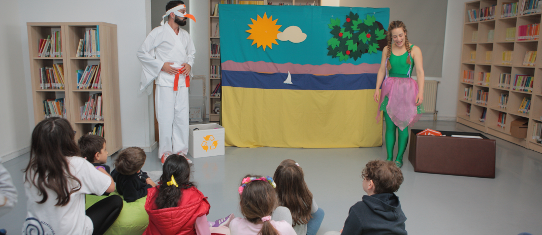 A girl dressed in green and a man wearing a karate suit, perform in front of sitting kids